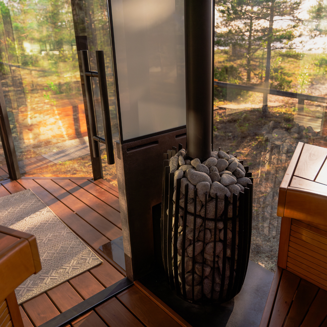 Wood-burning stove on a wooden deck with a view of trees and a fence.
