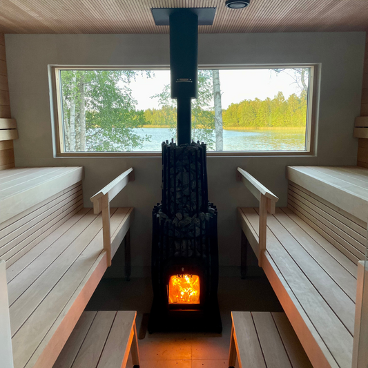 Sauna interior with wooden benches and a lit stove, featuring a window view of a lake and trees.
