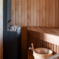 Cozy sauna interior with wooden walls and bench, a heater filled with smooth stones, and a wooden bucket and ladle, creating a warm, serene atmosphere.