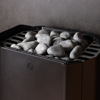 A sauna heater filled with smooth gray stones against a dark wall. The metal grate supports the stones, creating a warm, tranquil atmosphere.