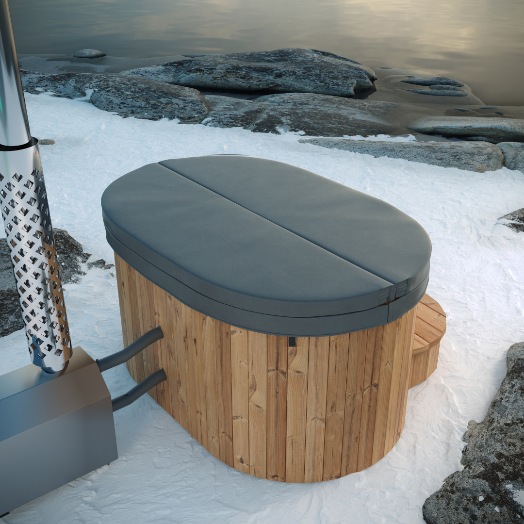 Wooden hot tub with a closed gray cover sits on snow by a peaceful lake. Surrounding rocks and calm water convey a serene, wintery feel.