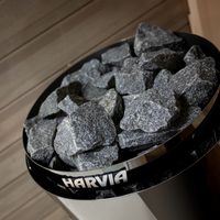 Black container filled with gray stones labeled 'Harvia' on a wooden floor.
