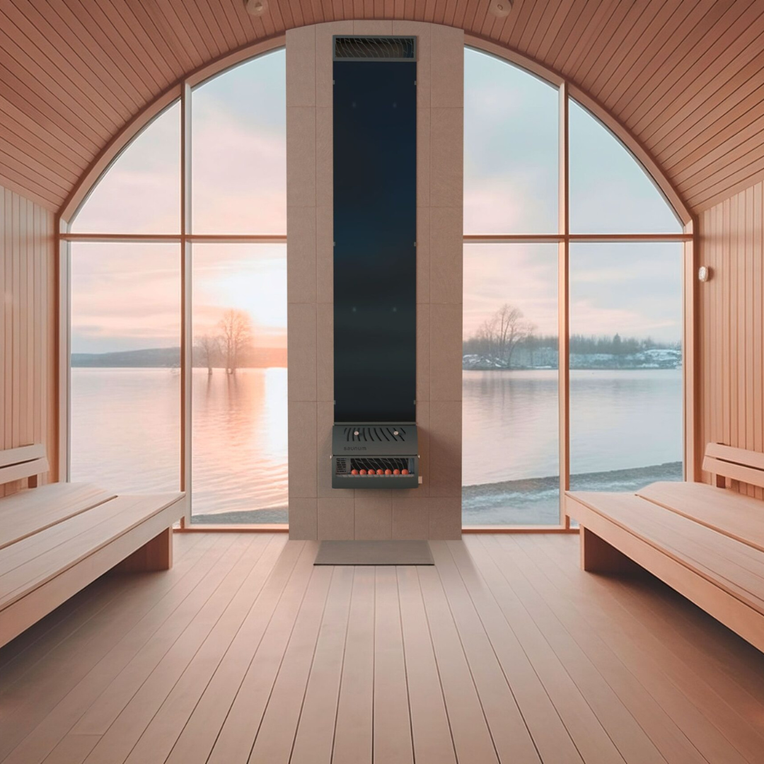 A modern sauna heater, the Saunum Base, mounted on the wall of a sauna room with a scenic window overlooking a body of water and trees. The room features wooden benches and a sleek design.