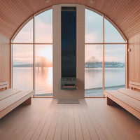 A modern sauna heater, the Saunum Base, mounted on the wall of a sauna room with a scenic window overlooking a body of water and trees. The room features wooden benches and a sleek design.