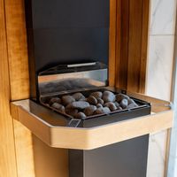 A modern sauna heater with smooth gray stones is mounted on a wooden corner. The warm tones create a relaxing, inviting atmosphere.