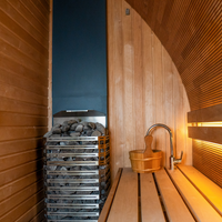 Wooden sauna interior featuring a stone heater, a wooden bench, and a water bucket with ladle. Warm lighting creates a relaxing atmosphere.