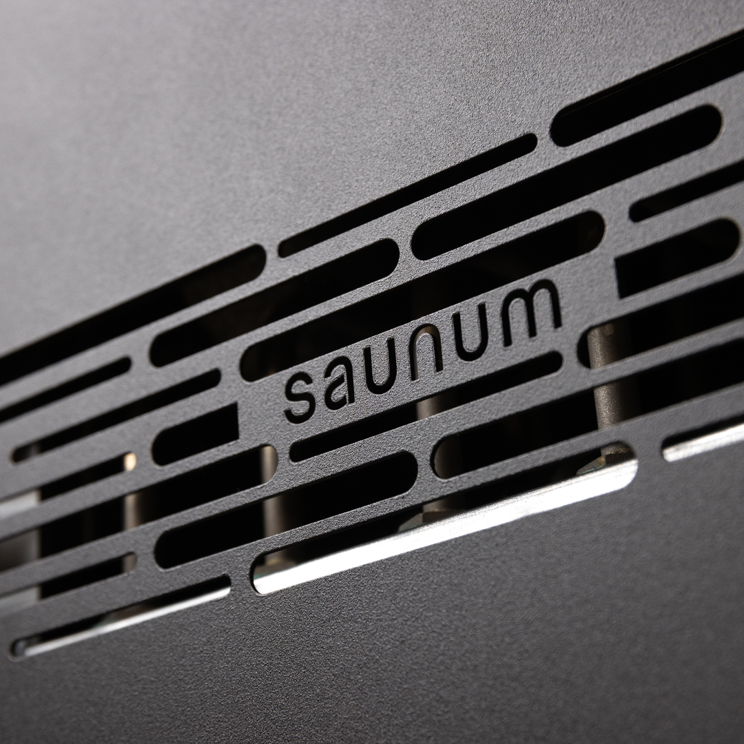 Close-up of a black metal surface with horizontal slits, showing the word "saunum" cut into the design. The tone is sleek and modern.