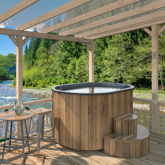 An outdoor wooden ice bath tub with ergonomic seats, situated on a deck with a scenic view of nature in the background. Includes insulated cover and wooden steps.