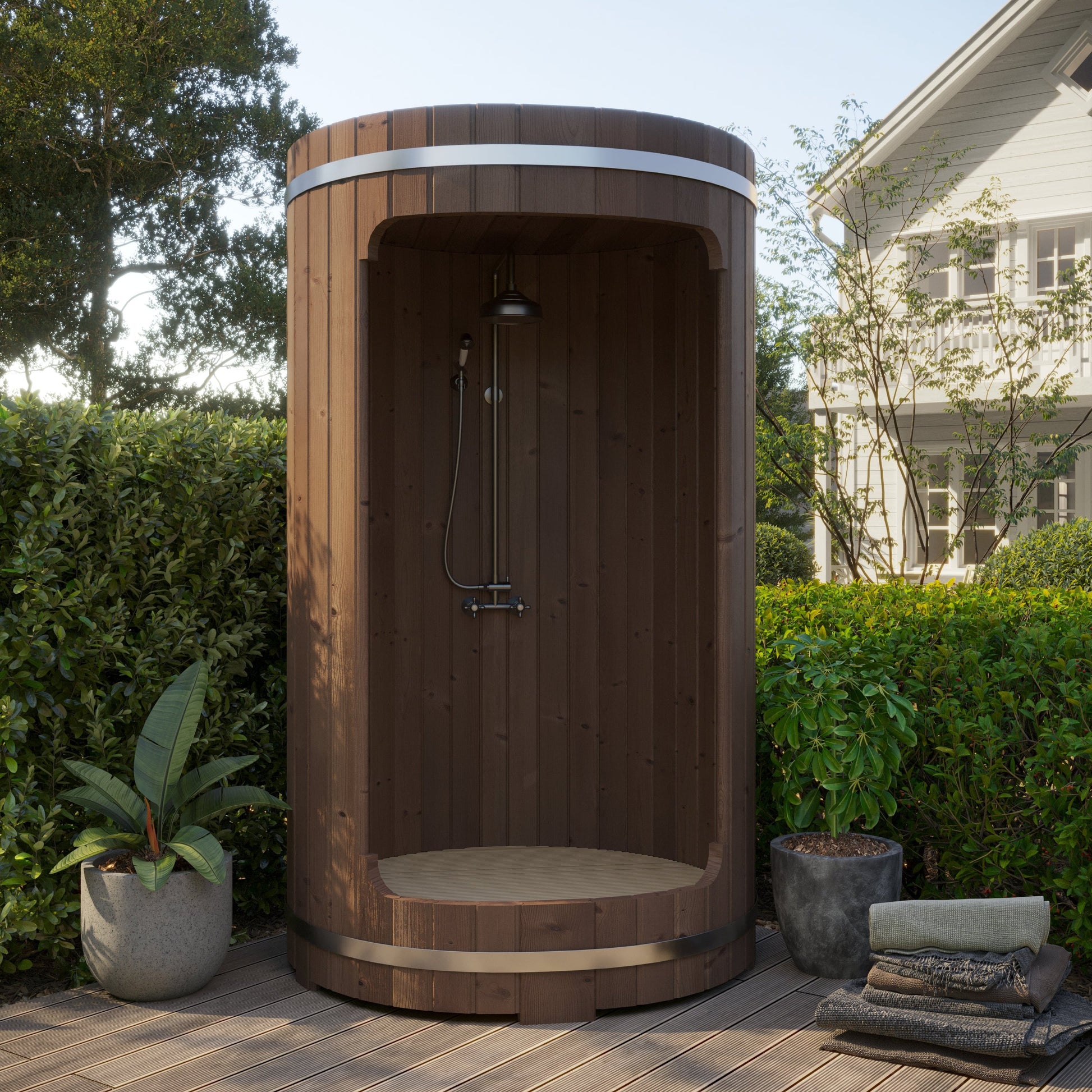 Wooden outdoor shower enclosure in a garden setting with plants and a house in the background.