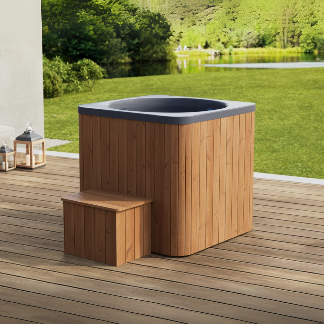 An ice bath tub with a wooden exterior, black interior lining, accompanied by a wooden chiller and a small wooden bench, set on a wooden deck with a scenic background.